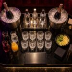 An overhead view of a reserved nightclub VIP table set with champagne and spirit bottles on ice, mixers, cut-crystal glassware and citrus garnish.